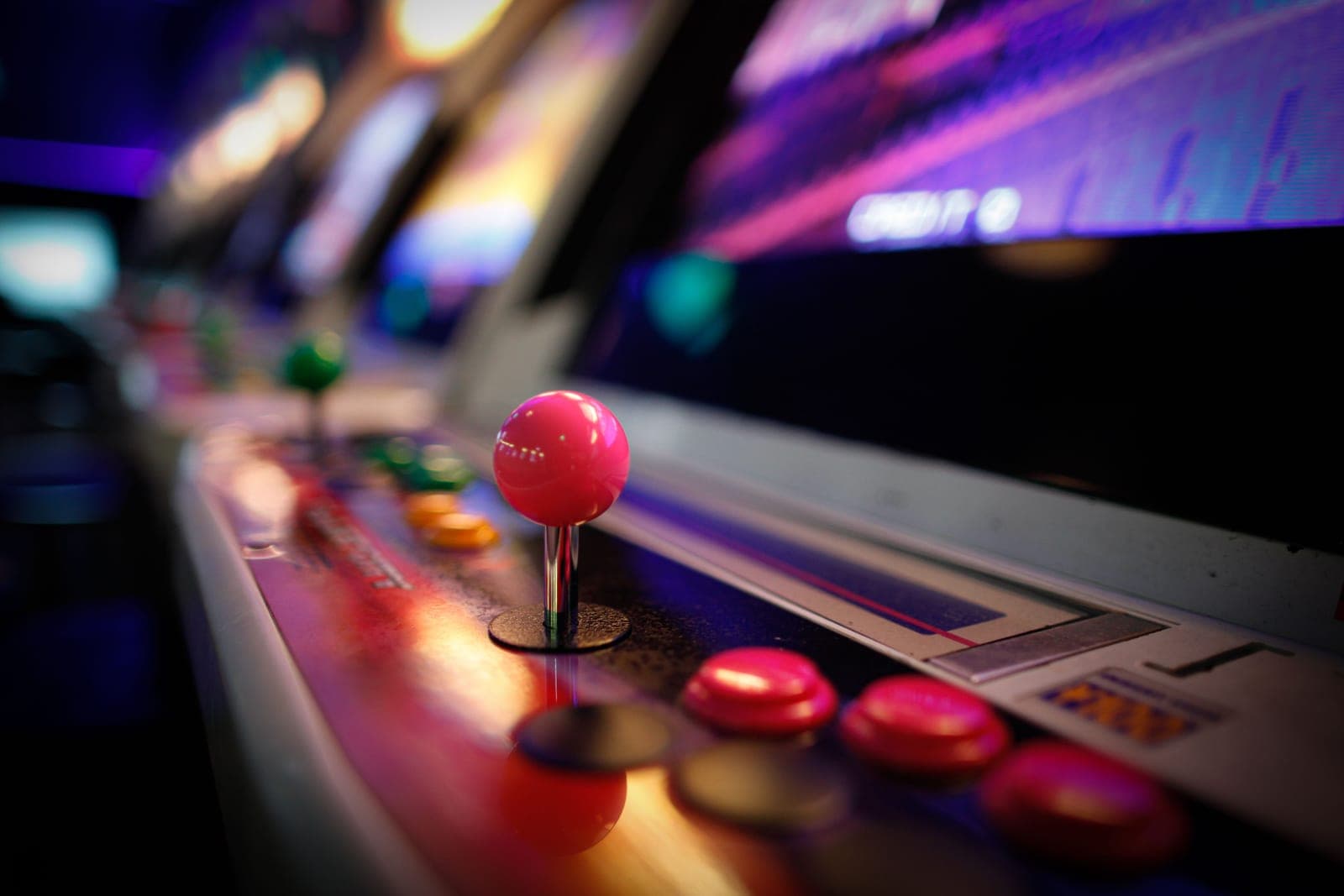 A row of upright arcade cabinets lit against a dark wall
