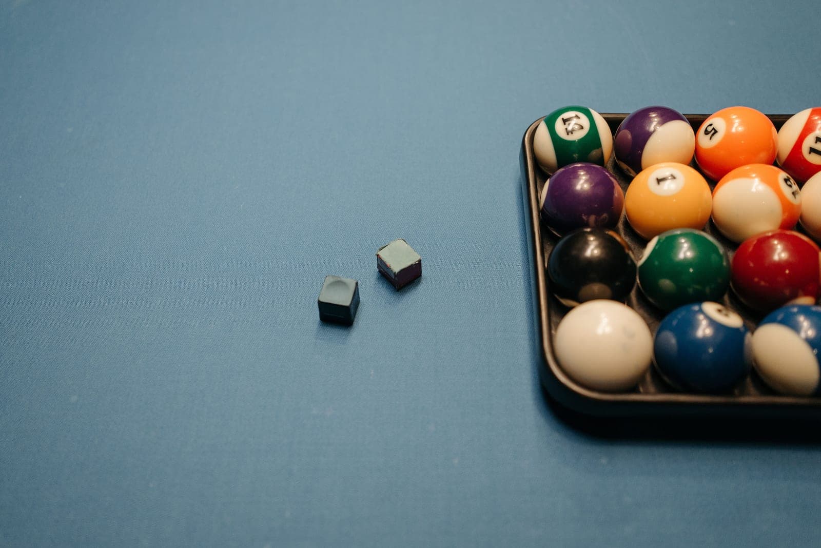 A cue tip and chalk resting on a billiard table rail