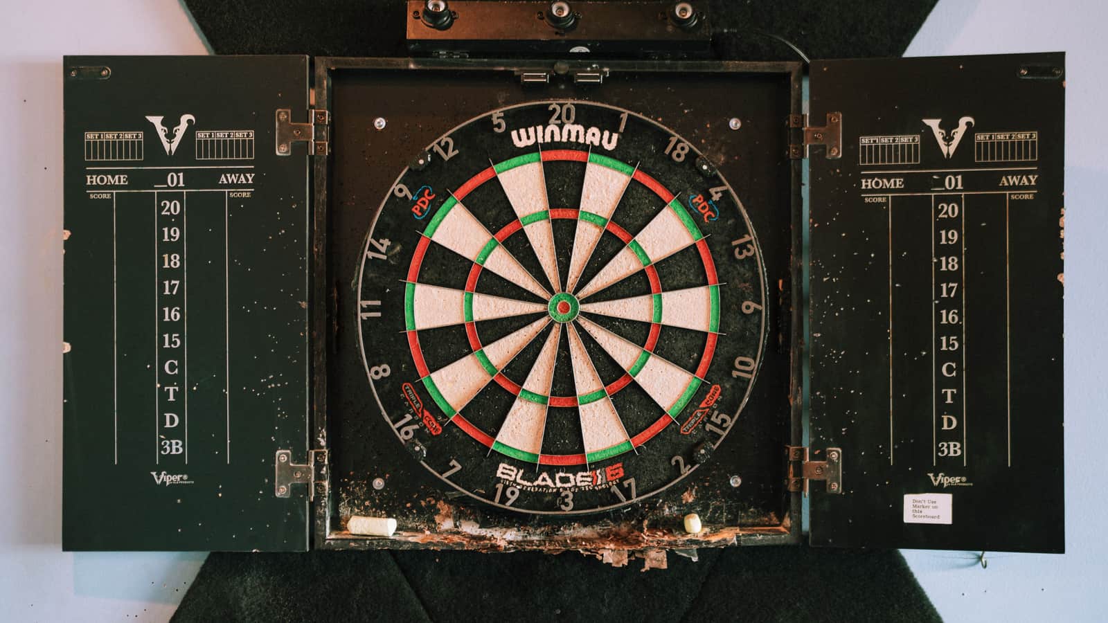 A dart board cabinet with its doors open, protecting the wall around the board