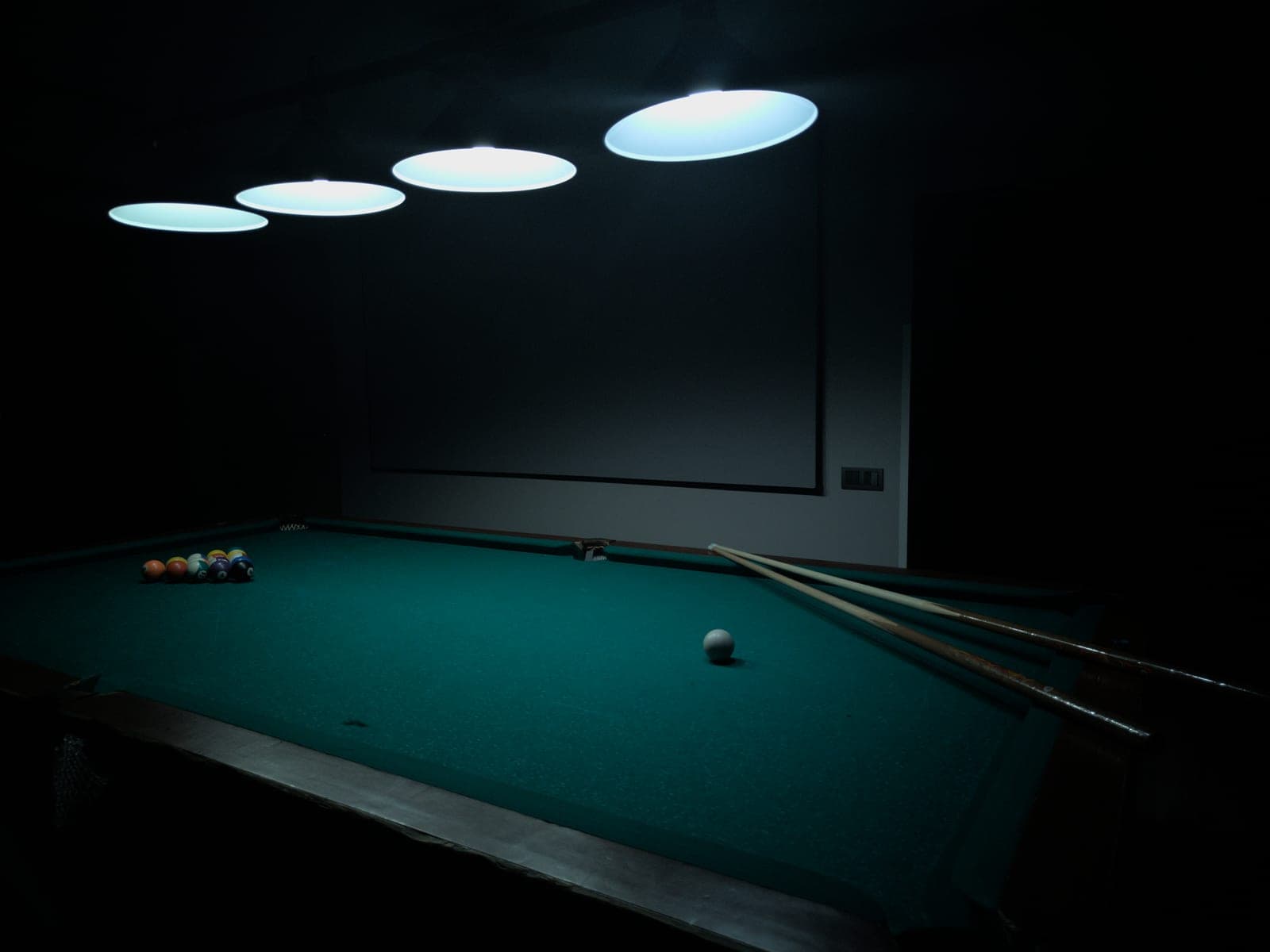A home billiard table lit by low pendants in a dark room, with clear cue space along both long rails