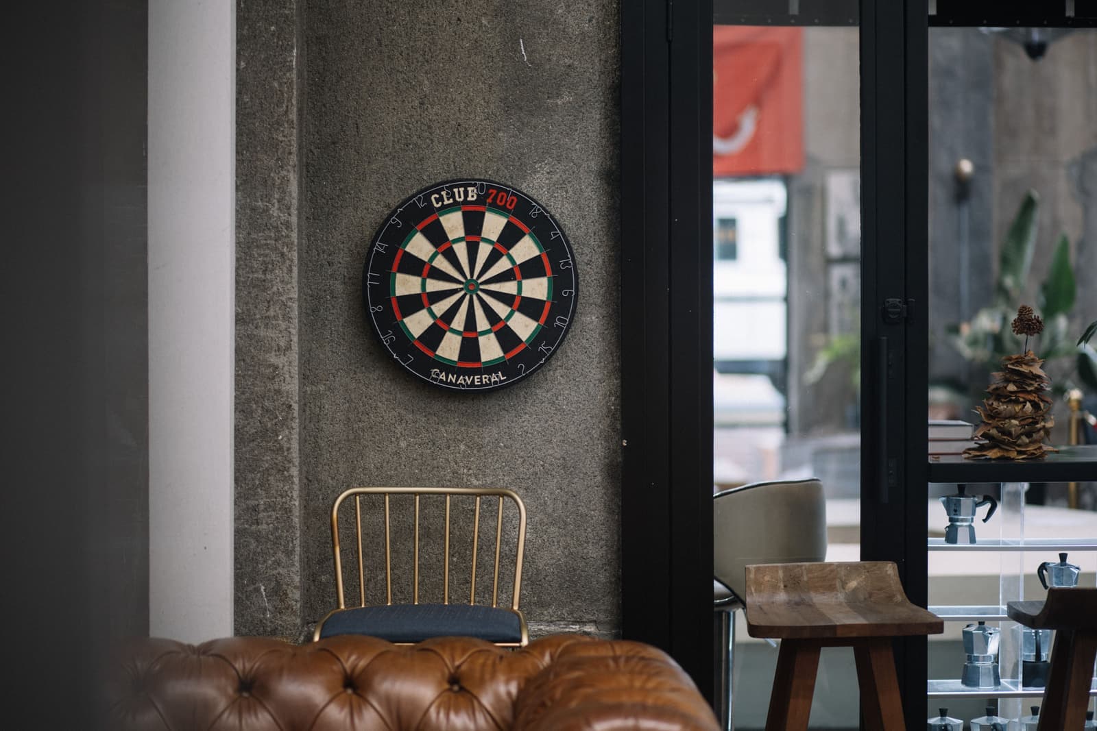 A bristle dart board mounted at regulation height on a dark wall with a throw-line mat on the floor