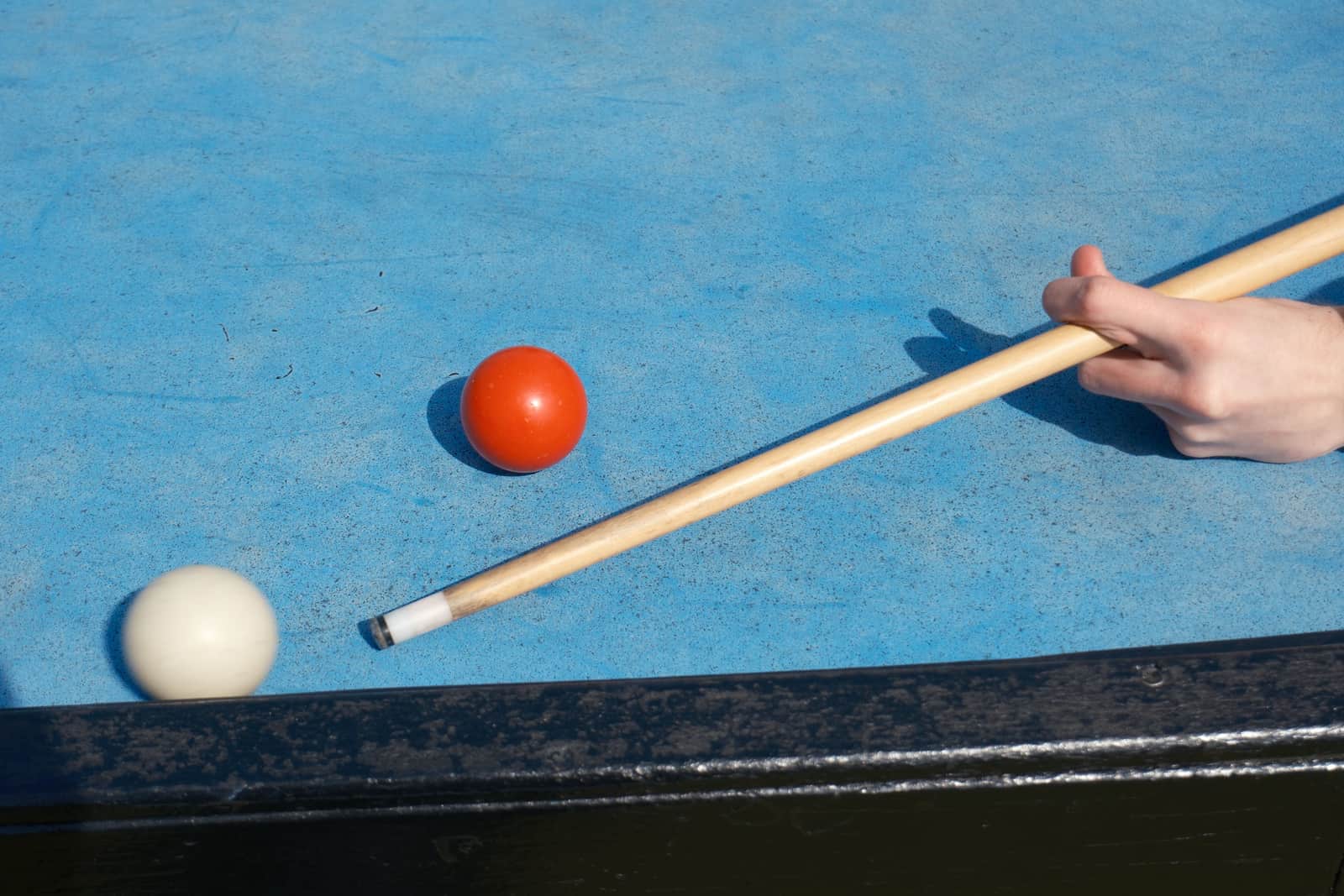A cue lined up along the length of a full-size pool table in a lit room