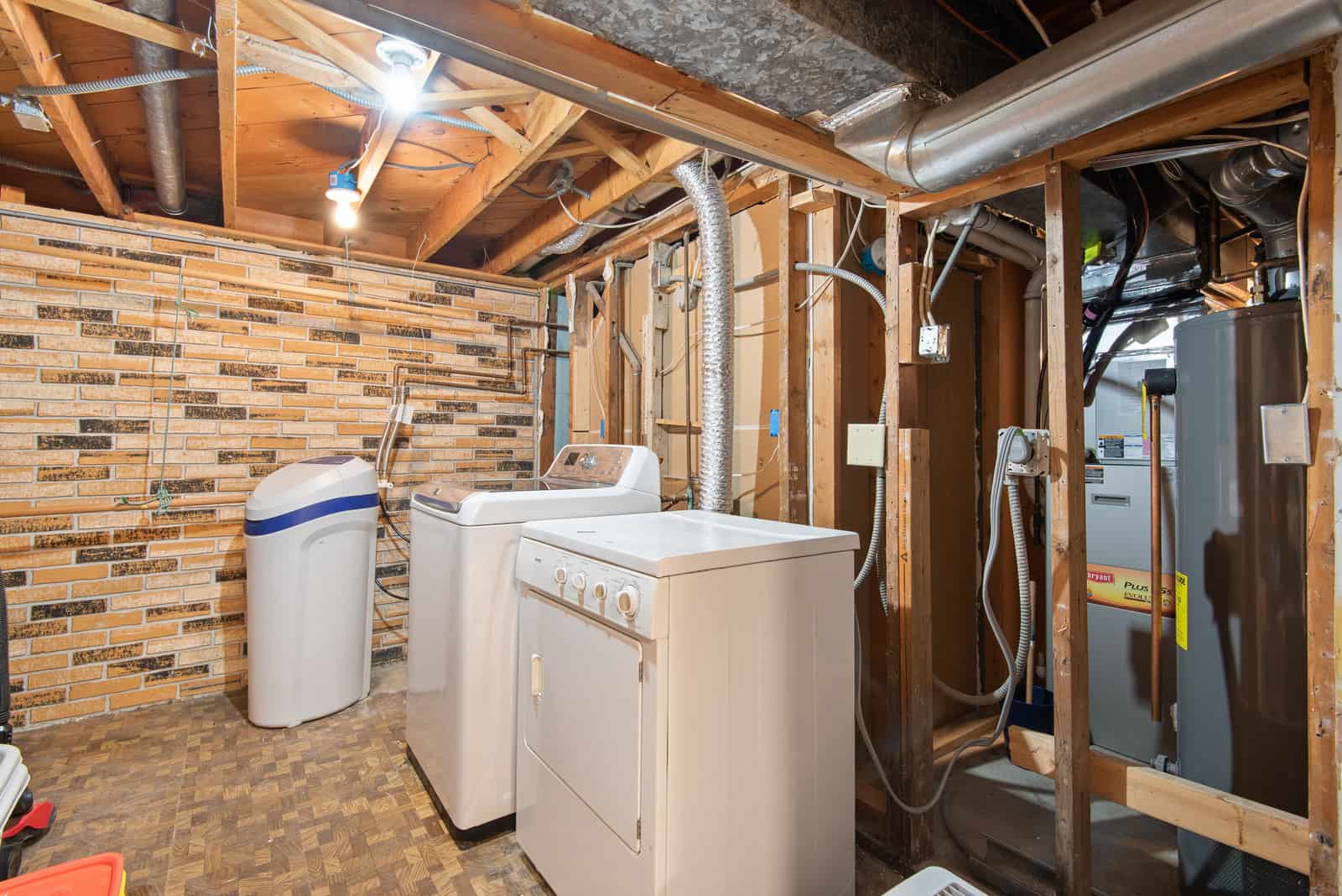 A basement ceiling with exposed ductwork and pipes running below the joists