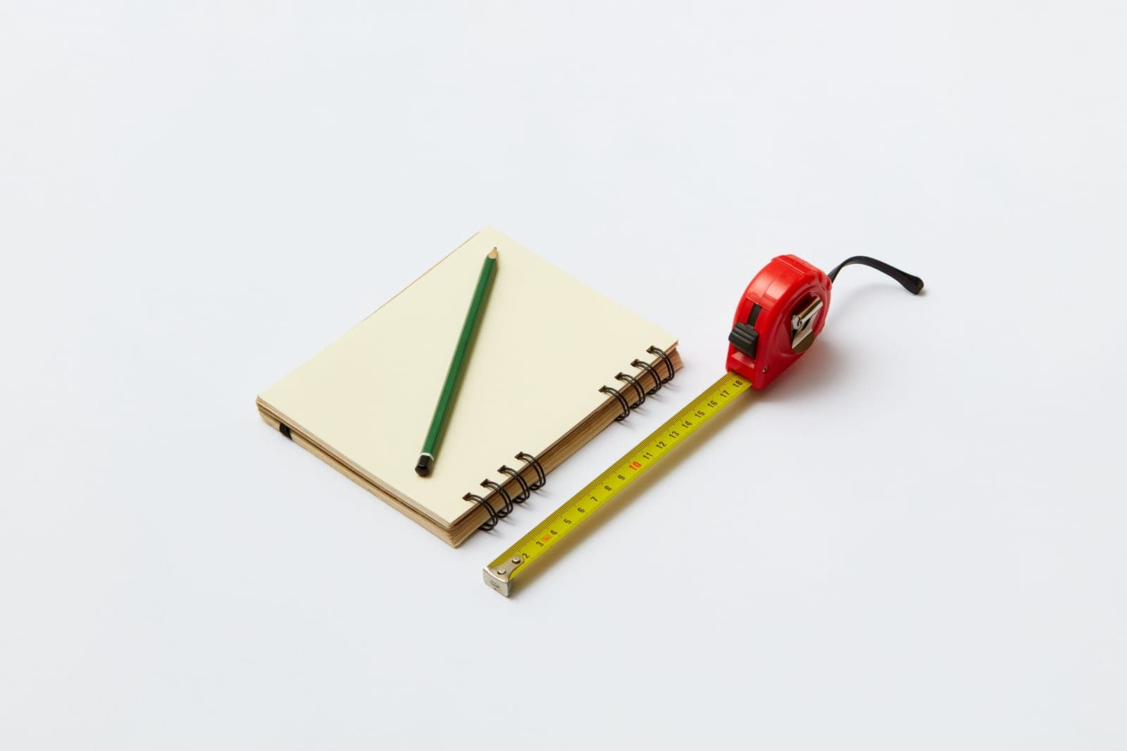 A tape measure, notebook and pencil on a workbench